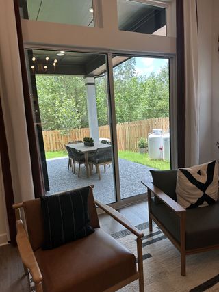 A cozy living area with stylish armchairs, large windows, and a view of the fenced backyard patio with outdoor seating.