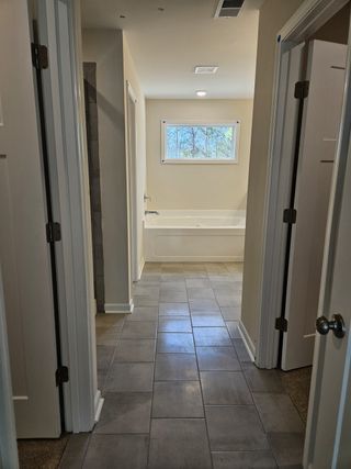 Long hallway leading to a bathroom with a large tub, tiled floor, and natural light from a window.