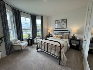 A cozy bedroom with a metal bed frame, elegant armchairs, and large windows draped with patterned curtains.