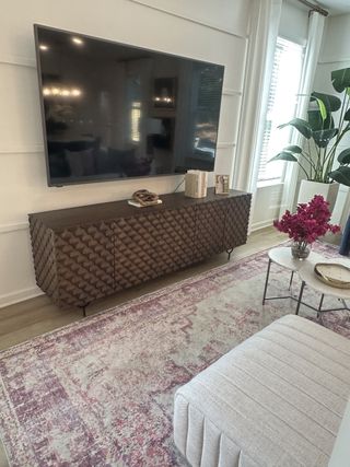 A stylish living area with a textured cabinet, large TV, patterned rug, and elegant decor, creating a cozy and inviting atmosphere.