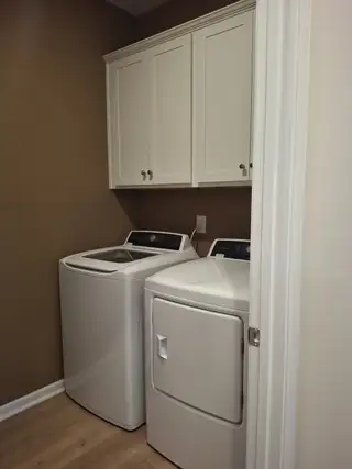 Model Home A sleek laundry room with a washer, dryer, white cabinetry, and beige walls offering functional style.