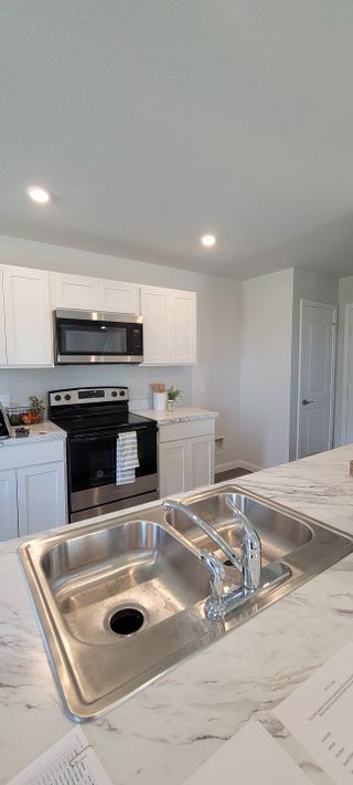 Model Home A modern kitchen with sleek white cabinets, stainless steel appliances, and a marble-look countertop.