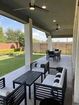 Model Home A stylish patio with sleek black furniture, ceiling fans, and a spacious lawn, perfect for outdoor relaxation.