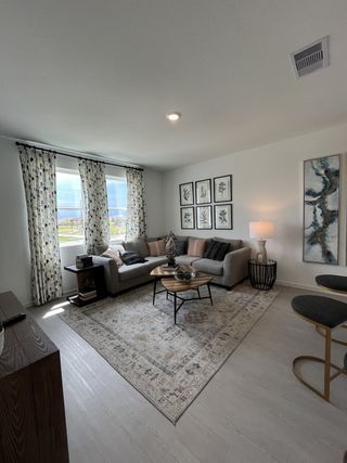 A cozy living room with a gray sectional, patterned rug, elegant artwork, and natural light from large windows.