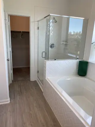 Model Home A modern bathroom with a glass-enclosed shower, a spacious tub, and elegant wood flooring.