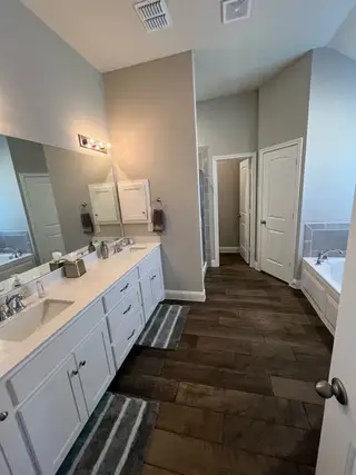 A spacious bathroom with dual sinks, dark wood flooring, and a modern bathtub for ultimate relaxation.