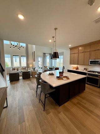 An open-concept kitchen with a large island, modern lighting, and ample natural light leading to a cozy living area.