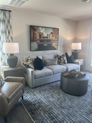 Model Home A cozy living room with a plush sofa, patterned cushions, and stylish decor, featuring a vintage car wall art.
