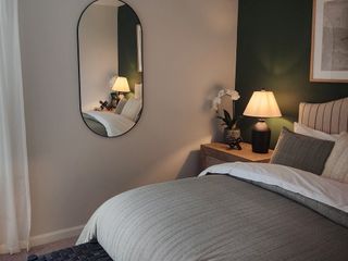 A cozy bedroom with a striped comforter, wood nightstand, modern lamp, and decorative mirror.