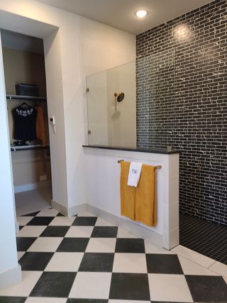 A chic bathroom with a black and white checkered floor, glass shower, and stylish black brick wall accents.
