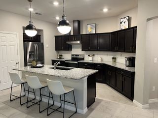 A modern kitchen with dark wood cabinetry, a sleek granite island, and stylish pendant lighting over white tile flooring.