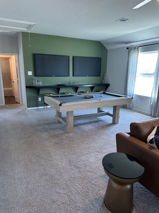 A cozy game room featuring a stylish pool table, dual TVs, and comfy seating, perfect for entertainment and relaxation.