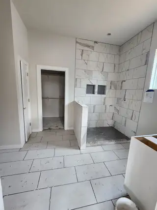 Model Home A modern bathroom featuring marble-tiled walls and floors, with a spacious walk-in shower and a nearby closet doorway.