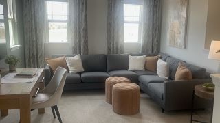A cozy living area featuring a plush gray sectional, elegant artwork, and light-filled windows adorned with patterned drapes.
