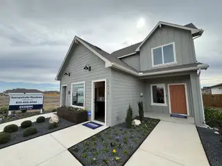 A charming gray model home with a warm orange door and lush landscaping in Saengerhalle Meadows by D.R. Horton (New Braunfels, TX).
