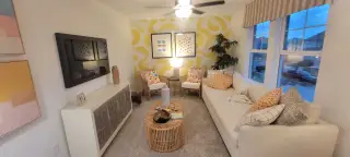 A cozy living room with a cream sofa, colorful art, and a wicker coffee table, highlighted by a bold yellow accent wall.