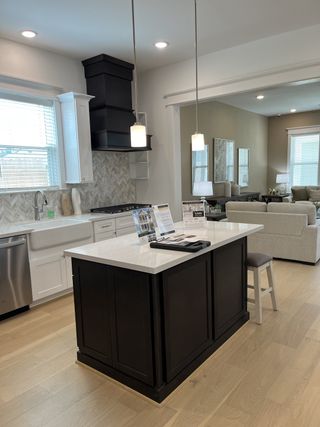 A modern kitchen with a sleek white island, black cabinetry, pendant lighting, and a cozy living space in view.