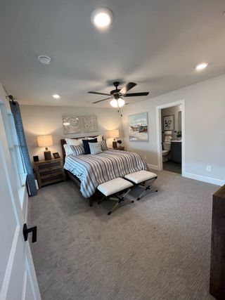 A cozy bedroom with a striped bedspread, ceiling fan, and elegant decor, leading to a connected bathroom.