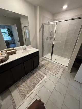 A modern bathroom featuring a sleek glass shower, dark vanity, and elegant tiled floor with cozy rugs.