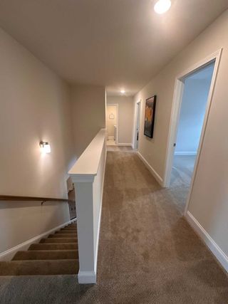 Model Home A cozy carpeted hallway with soft lighting and neutral walls, leading to bedrooms and adorned with wall art.