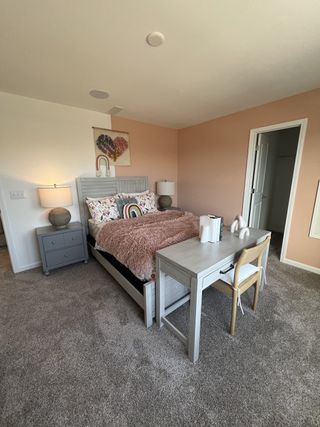 Cozy bedroom with a stylish gray bed, pink accent wall, and a functional desk area.