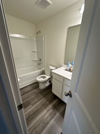 A compact bathroom with elegant wood-look flooring, a sleek vanity, and a pristine white bathtub.