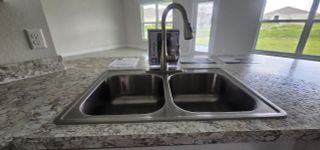 Model Home A modern kitchen with a dual stainless steel sink, speckled granite countertops, and large windows.