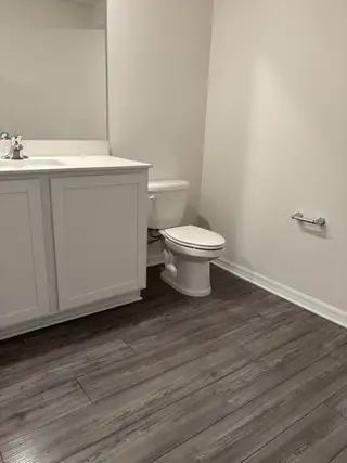 Model Home A modern bathroom featuring sleek wood-style flooring, a white vanity, and minimalist fixtures.