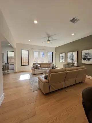Model Home A cozy living room featuring beige leather sofas, wood floors, large windows, and contemporary wall art.