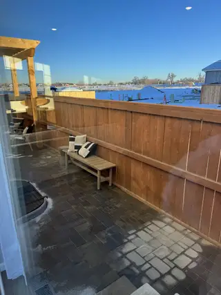 A cozy patio with a wooden fence, bench seating, and views of a snowy landscape under a clear blue sky.