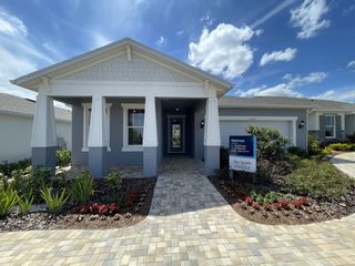 A stunning model home with a charming front porch, crisp blue exterior, and lush landscaping in Del Webb Minneola by Del Webb (Minneola, FL).