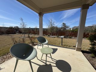 A cozy patio with modern chairs overlooks a spacious backyard and scenic view under a clear blue sky.