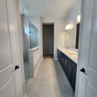 A sleek bathroom with a spacious glass shower, dark double vanity, and bright lighting.