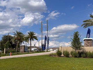 The grand entrance of Cascades by Lennar (Davenport, FL) welcomes residents with lush landscaping, palm trees, and elegant stone pillars.