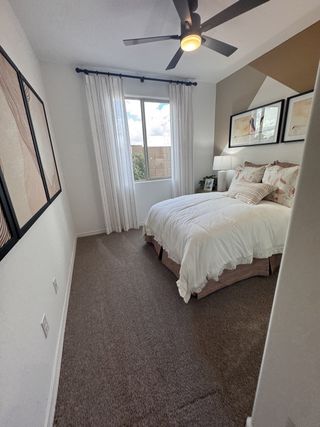 A cozy bedroom with modern geometric decor, plush carpeting, and a ceiling fan for comfort and style.