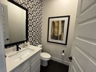A chic half-bath with geometric black-and-white wallpaper, a sleek vanity, and a modern mirror.