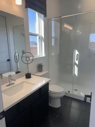 A sleek bathroom with a large glass shower, white vanity, black tiles, and modern lighting.