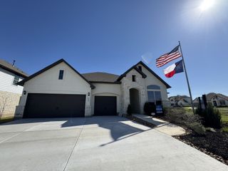 A modern home with a stone facade and dual flags, in Buffalo Crossing by Bellaire Homes (Cibolo, TX).