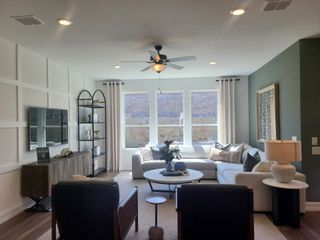 Model Home A cozy living room with a sectional sofa, stylish shelving, and elegant decor, enhanced by natural light and a ceiling fan.