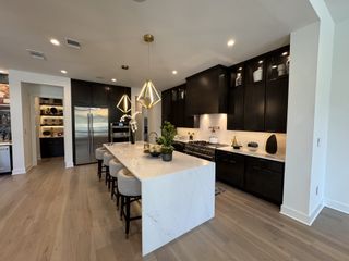 A spacious kitchen with a large island featuring a white countertop, dark cabinetry, and gold pendant lighting, complemented by stainless steel appliances and light wood flooring.