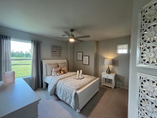 A cozy bedroom with soft gray walls, elegant white furniture, and a large window offering a serene view of the outdoors.
