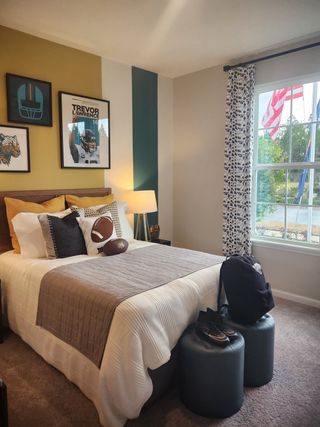 A cozy bedroom with sports decor, featuring a stylish accent wall, plush bedding, and natural light from a large window.