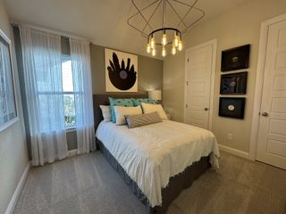 Model Home A cozy bedroom with modern lighting, a plush bed, vinyl wall art, and sheer curtains.