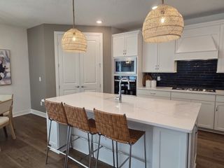 A modern kitchen with a marble island, wicker lighting, sleek cabinetry, and a cozy dining area.