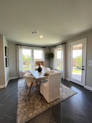 Model Home A elegant dining area with a sleek wooden table, modern chairs, large windows, and stylish decor on a patterned rug.