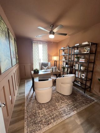 A cozy home office with elegant decor, featuring a wooden desk, stylish chairs, bookshelves, and a patterned rug.