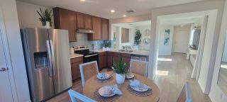 Model Home A bright kitchen and dining area in a Medina Crossing home, featuring dark wood cabinets, stainless steel appliances, a round dining table, and an open layout leading to the living space (Von Ormy, TX).