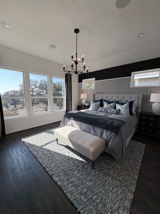 Model Home A modern primary bedroom with a vaulted ceiling, black chandelier, and floor-to-ceiling windows in Esperanza by Scott Felder Homes (Boerne, TX).