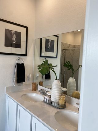 A modern bathroom with dual sinks, a large mirror, stylish decor, and a chic monochrome print on the wall.