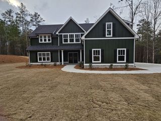 Model Home A spacious green farmhouse-style home with black shutters, white trim, and a curved walkway leading to the entrance.